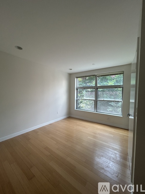 A room with wooden flooring and a window with a view of trees.