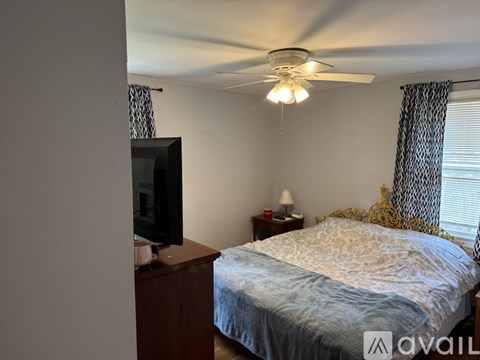 A bedroom with a bed, a television, and a ceiling fan.