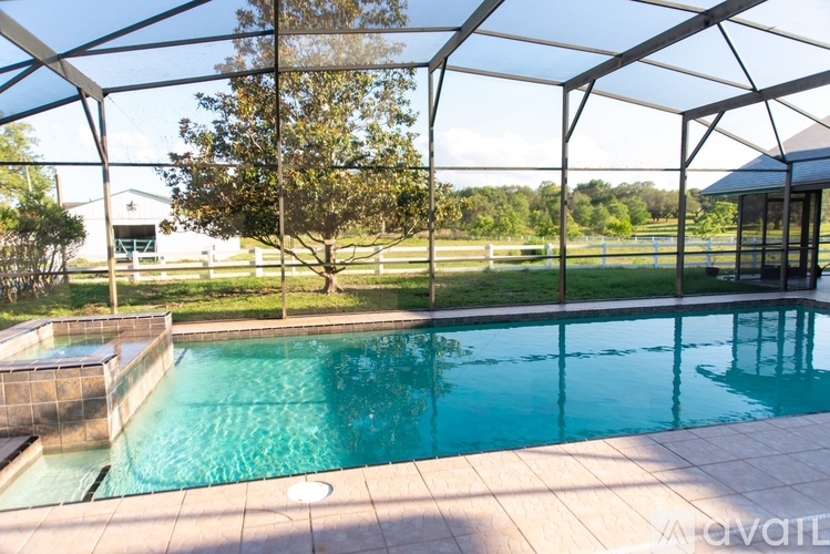 A pool with a glass enclosure and a tree in the background.