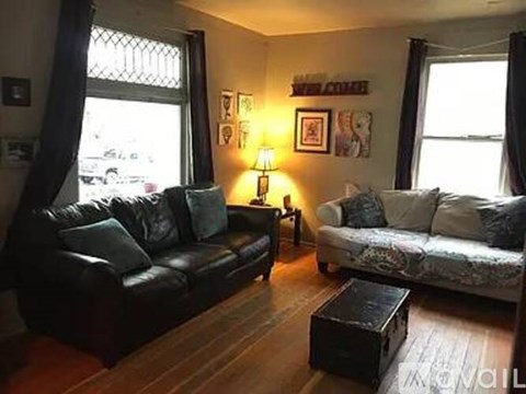 A living room with a black leather couch and a patterned sofa.