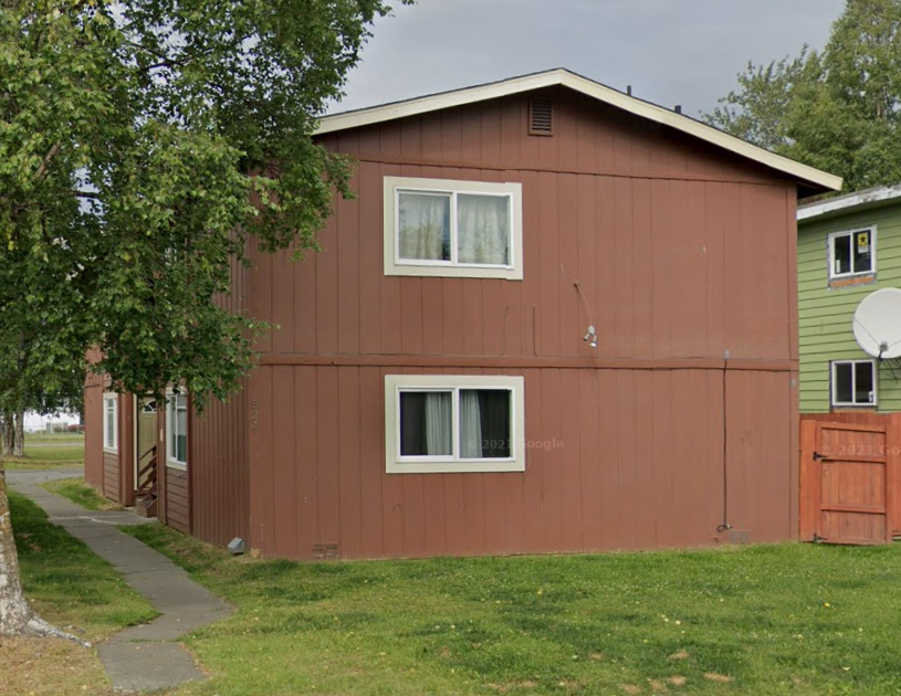 A brown house with a green house in the background.