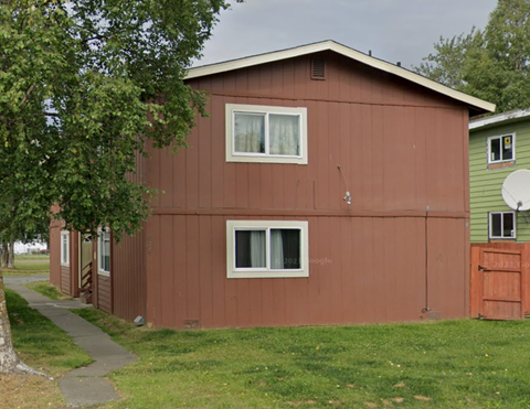 A brown house with a green house in the background.
