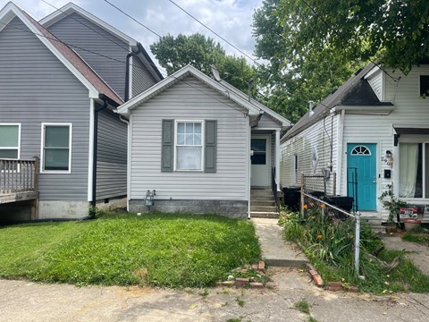 A small grey house with a blue door is surrounded by other houses.