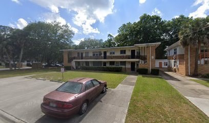 A red car is parked in a parking lot in front of a building.