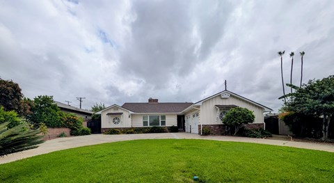 A house with a white exterior and a grey roof is surrounded by a green lawn.