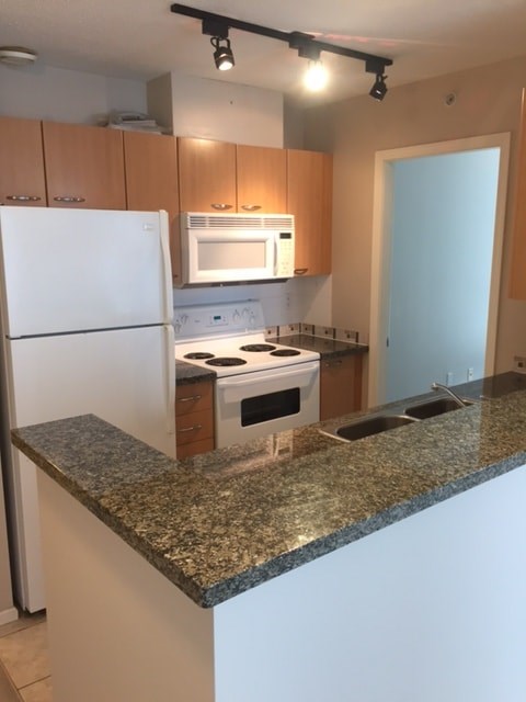 A kitchen with granite countertops and white appliances.