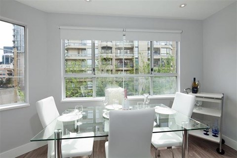 A glass dining table with four chairs in front of a window with a view of a building.