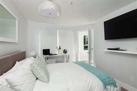 A bedroom with a bed, a desk with a laptop, and a television on the wall.