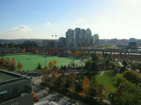 A cityscape with a green field in the foreground and buildings in the background.
