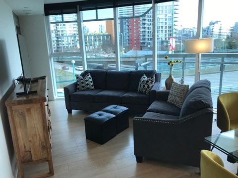 A black couch with a grey pillow and a black ottoman in a room with a large window.