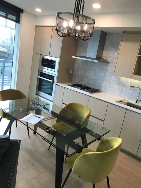 A modern kitchen with a glass table and yellow chairs.