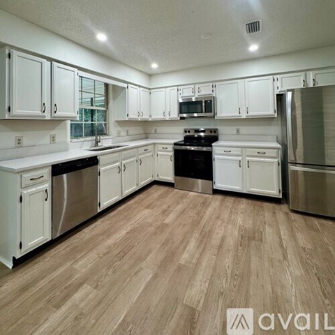 A kitchen with white cabinets and wooden floors.
