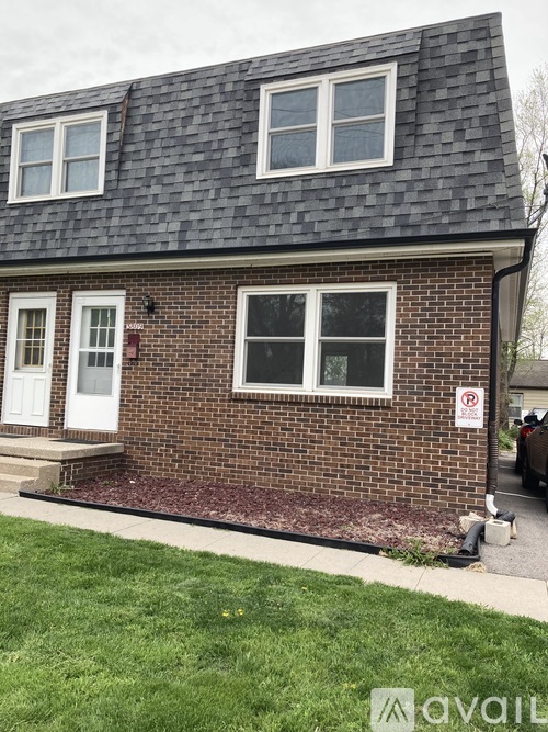 A brick house with a white door and a no parking sign on the right.