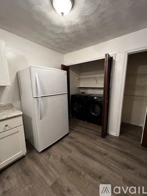 A white refrigerator stands in a kitchen with a washing machine in the background.