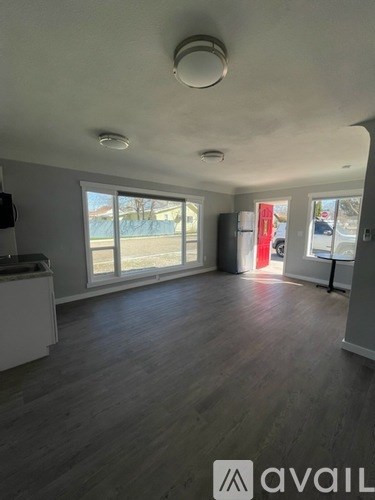 A spacious room with wooden flooring and a large window overlooking a parking lot.