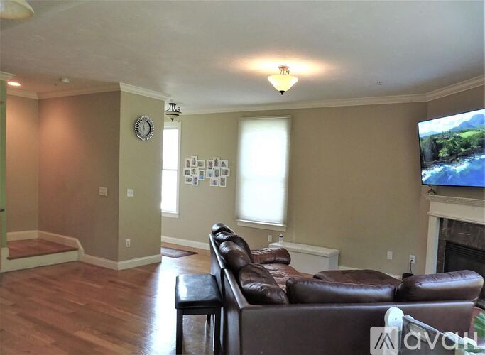 A living room with a brown leather couch and a flat screen TV mounted on the wall.