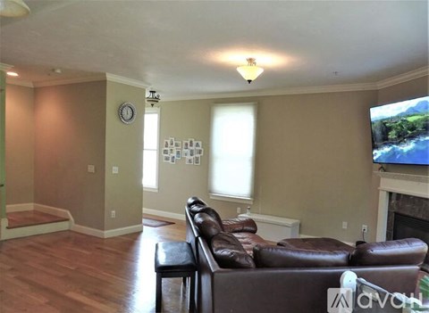 A living room with a brown leather couch and a flat screen TV mounted on the wall.