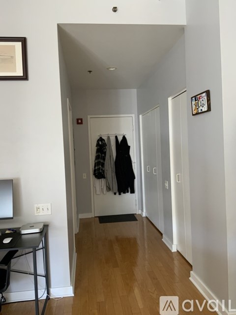 A hallway with a desk and a chair on the left and a coat hanging on the door on the right.