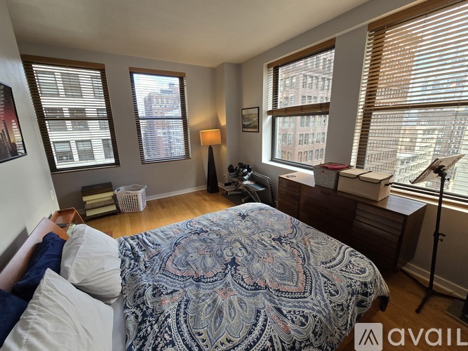 A bedroom with a bed in the center and a window with blinds on the right.