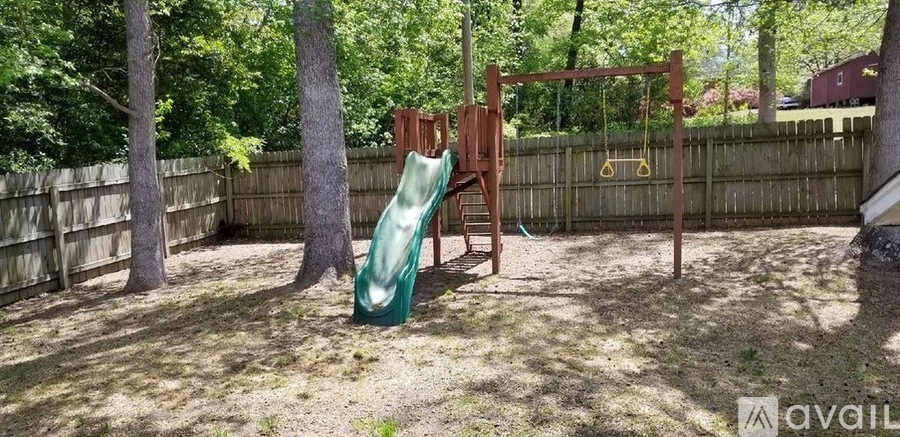A backyard with a green slide and a wooden swing set.