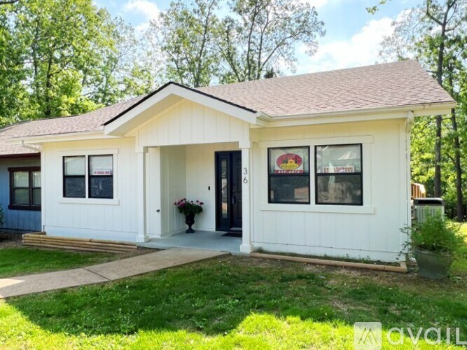 A white house with a black door and windows is surrounded by greenery.