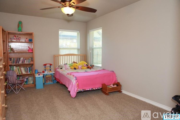 A child's bedroom with a pink bed and a bookcase filled with books.