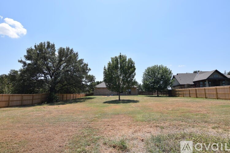 A grassy field with two trees and a house in the background.