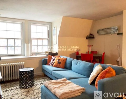 A living room with a blue couch and a black and white patterned ottoman.