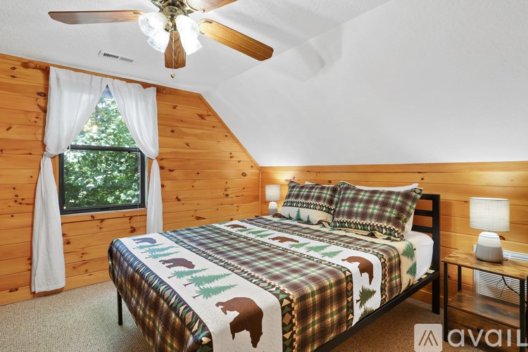 A bedroom with a bed, a ceiling fan, and a window with a view of trees.