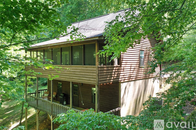 A wooden house with a balcony is surrounded by green trees.