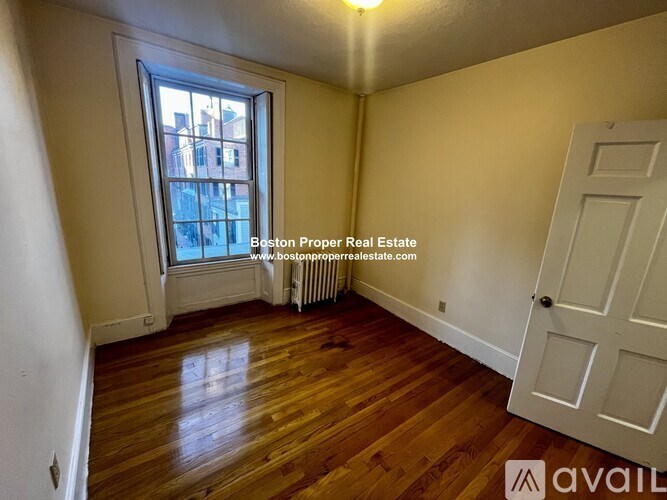 A room with wooden floors and a window showing a city view.