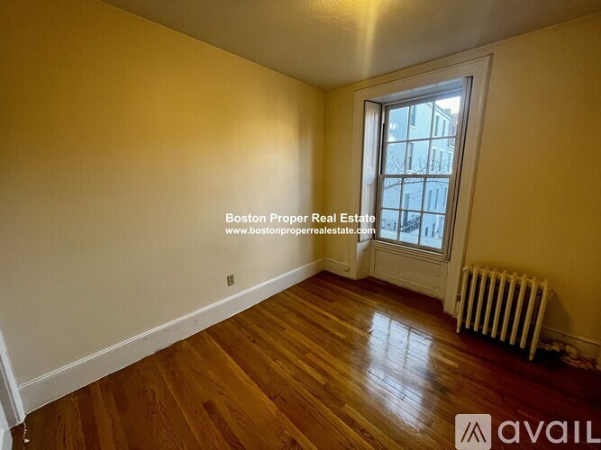 A room with wooden floors and a window with a view of a building outside.