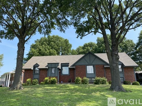A house with a red brick exterior and a large tree in front.