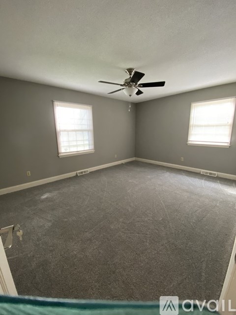 A room with a ceiling fan and two windows.