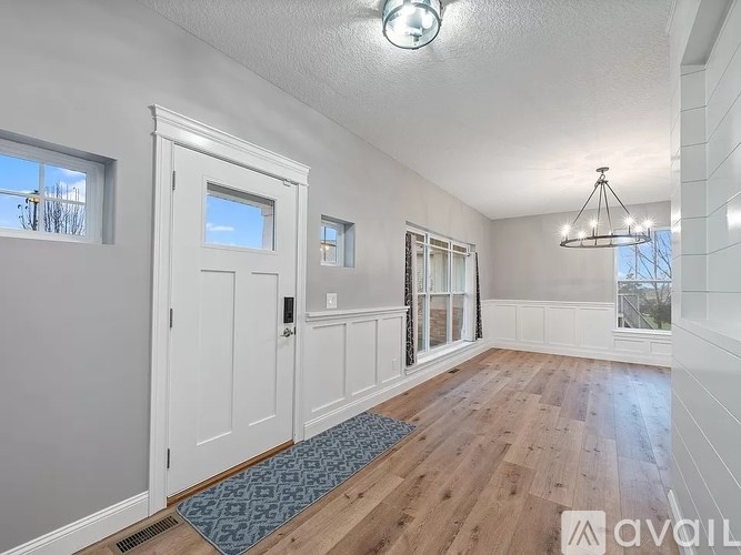 A room with a white door, a window with a view of trees, and a chandelier hanging from the ceiling.