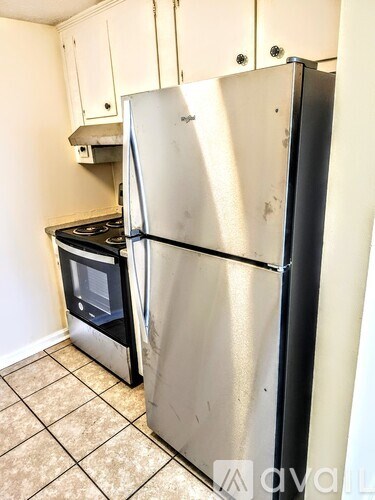 A silver refrigerator stands in a kitchen with a stove and white cabinets.
