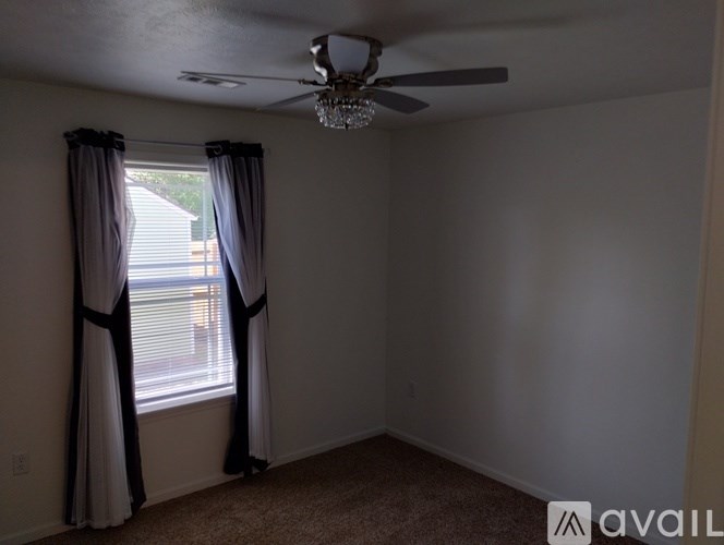 A room with a ceiling fan and a window with curtains.