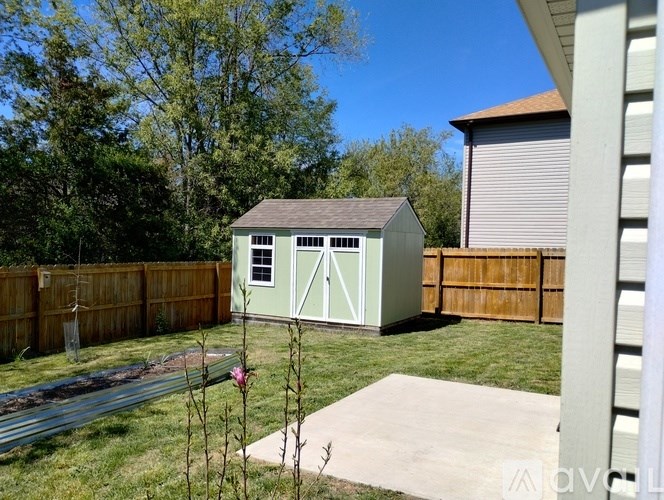 A green shed with a grey roof is in a backyard.
