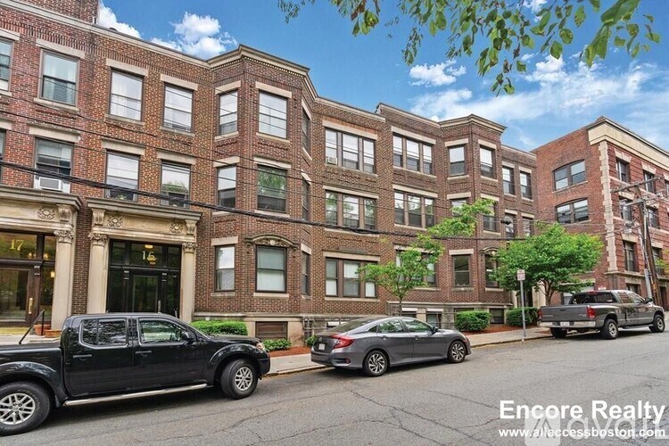 A street view of a row of red brick buildings with cars parked in front.