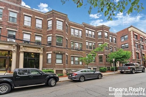A street view of a row of red brick buildings with cars parked in front.
