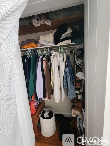 A white closet with clothes hanging and a trash can.