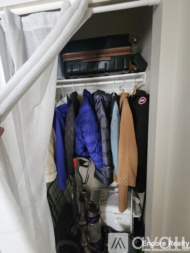 A white closet with clothes hanging and a vacuum cleaner on the floor.