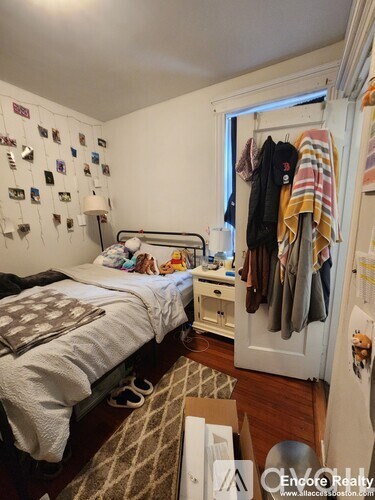 A bedroom with a bed, nightstand, and a closet with clothes hanging.