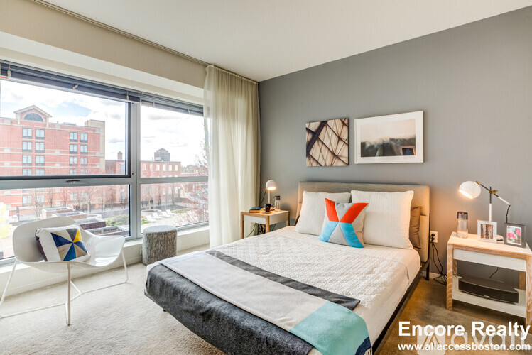 A bedroom with a large bed and a chair with a colorful cushion.
