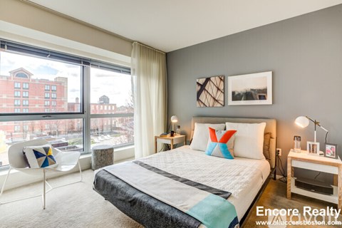 A bedroom with a large bed and a chair with a colorful cushion.