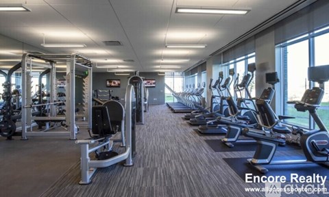 A well-lit gym with a variety of equipment including treadmills, elliptical machines, and weight machines.
