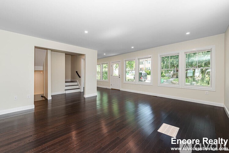 A spacious room with wood flooring and a staircase leading to another room.