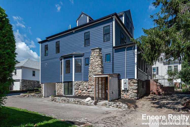 A blue house with a stone chimney is surrounded by greenery and a clear sky.