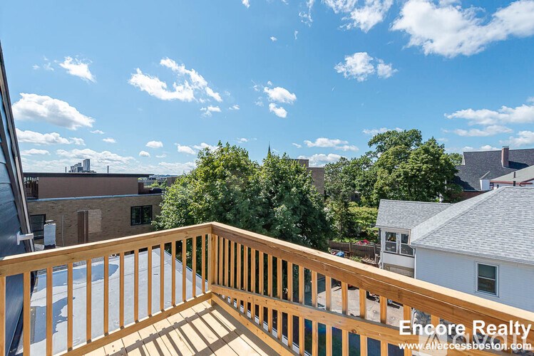 A balcony with a wooden railing overlooks a residential area.