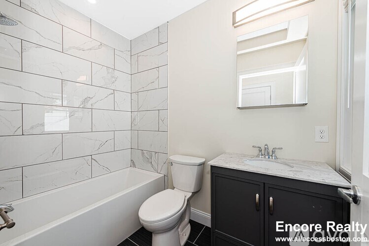 A white toilet sits next to a bathtub in a bathroom with marble tiles.
